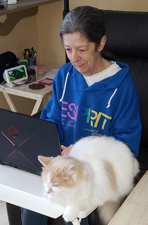 Jeannette working on her computer with Ginger her cat beside her.